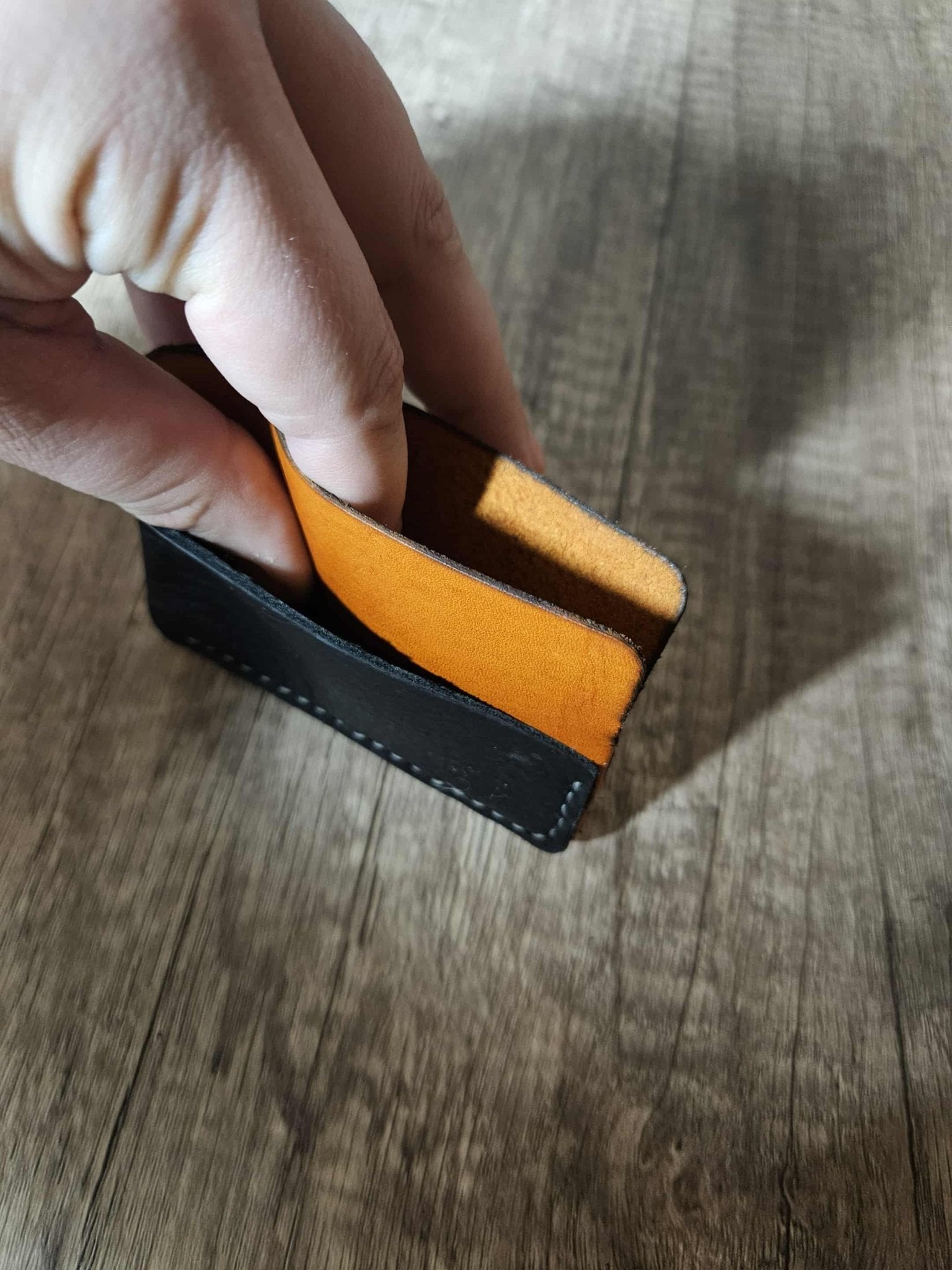 Hand holding a slim leather wrap wallet with black exterior and tan interior