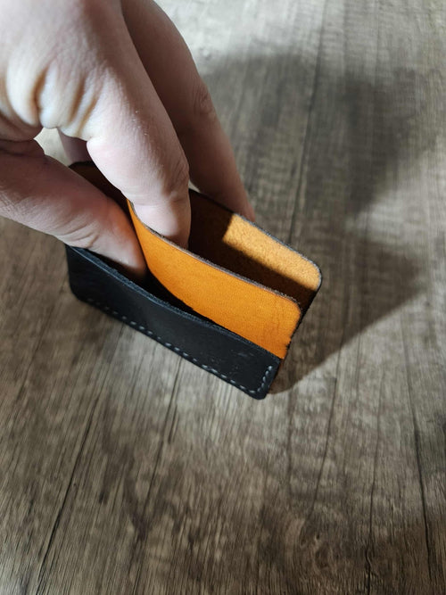 Hand holding a slim leather wrap wallet with black exterior and tan interior