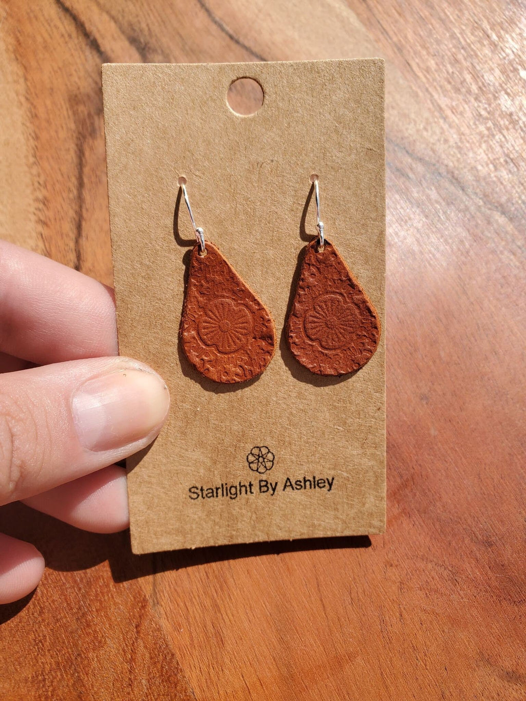 Brown leather teardrop earrings with embossed flower design and silver hooks
