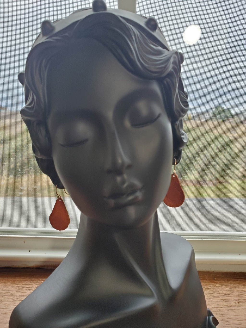 Rust red teardrop leather earrings with silver hook on model