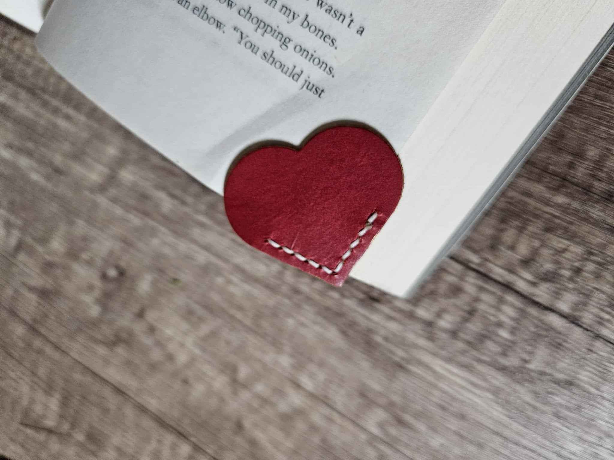 Red heart leather bookmark tucked in a book corner with white dashed stitching