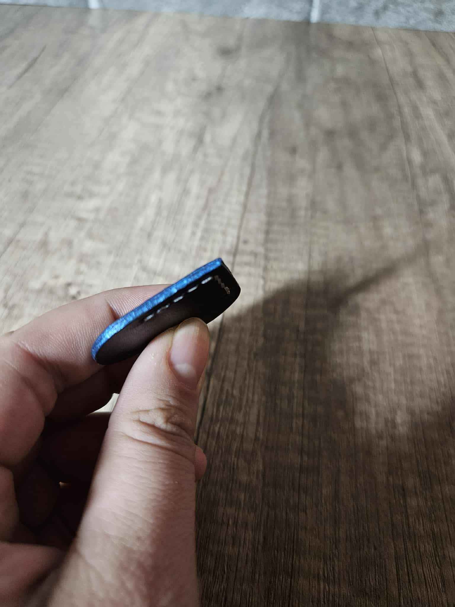 Black heart leather corner bookmark with blue stitching held in a hand