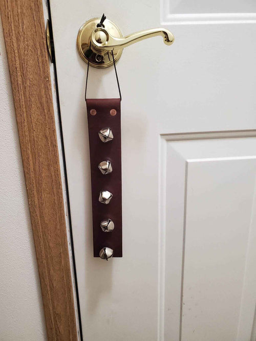 Leather doorbell strap with multiple round metal bells hanging from a doorknob