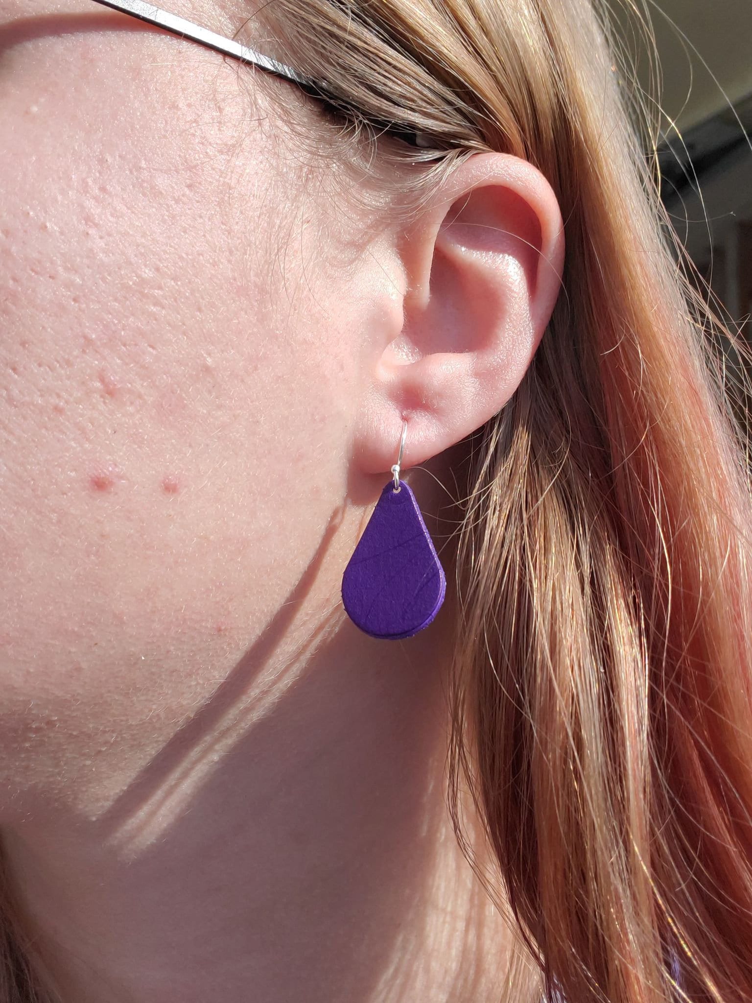 Purple teardrop leather drop earrings with silver hook, close-up on ear