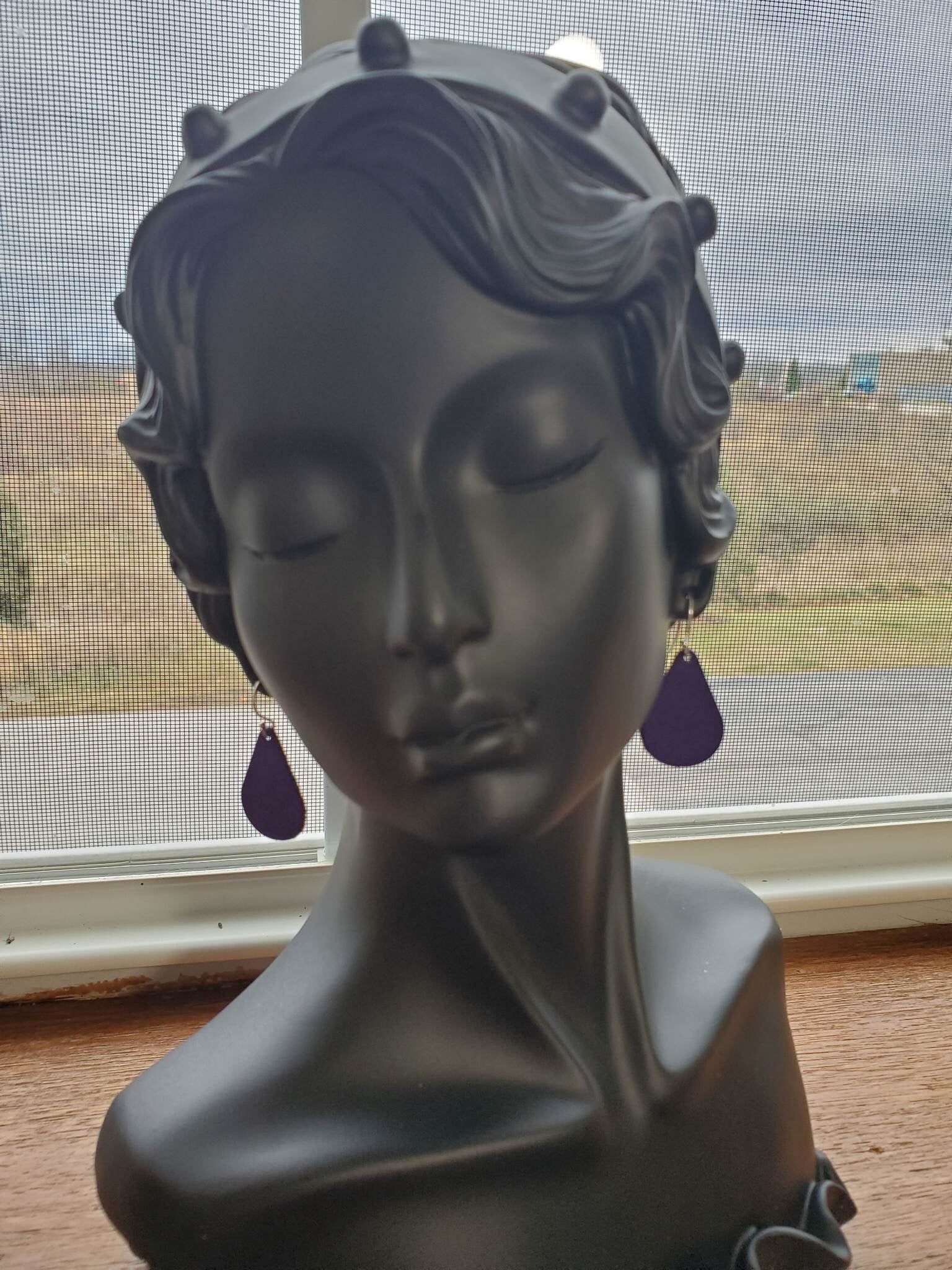 Pair of purple teardrop leather earrings with silver hooks, side view