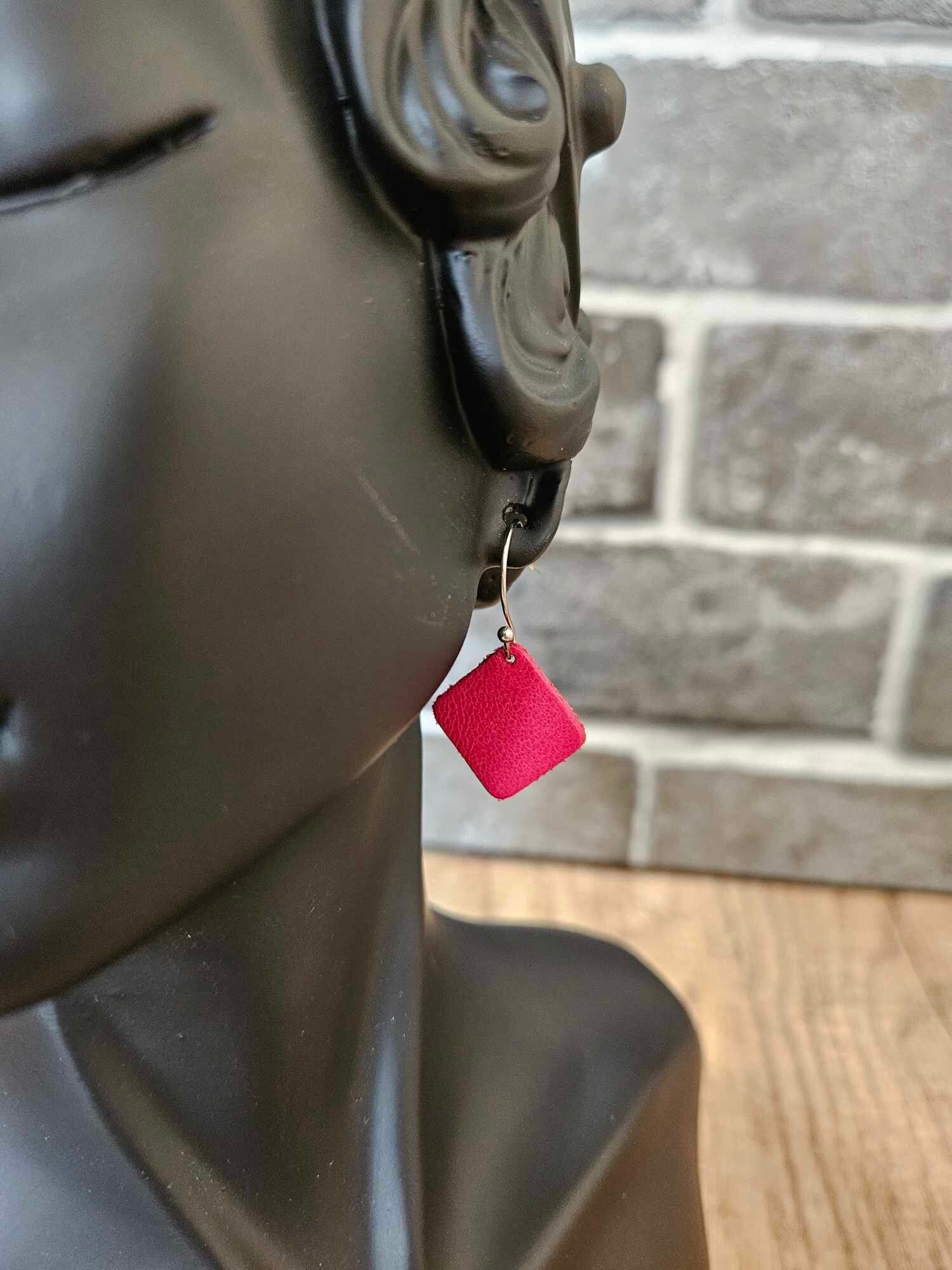 Red leather diamond earrings on silver hooks, shown close-up against brick wall