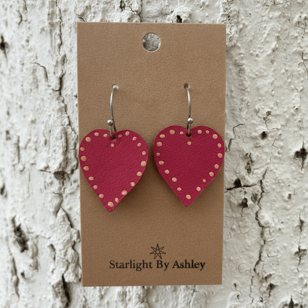Red heart leather earrings with gold dot details and silver hooks, on display card