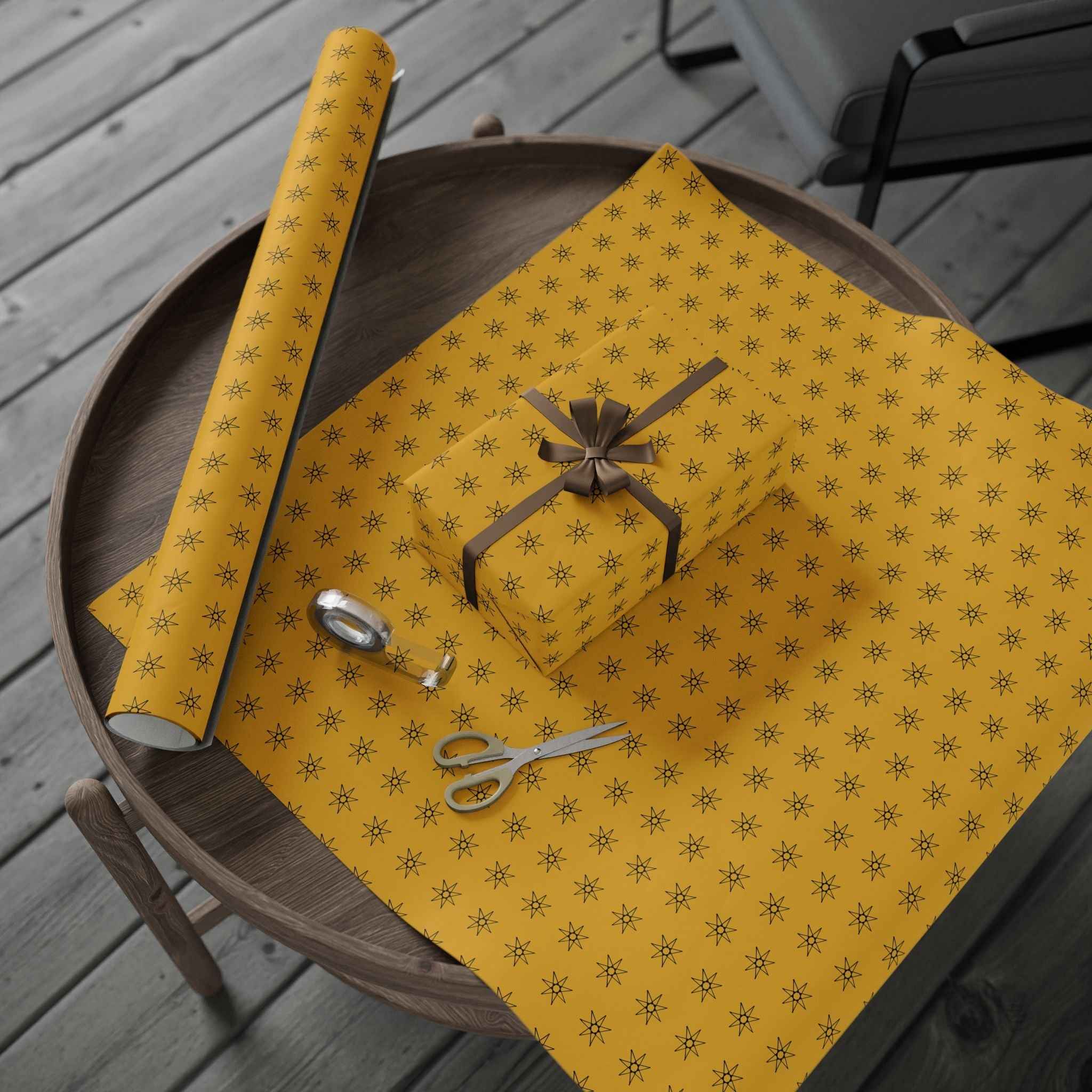 Yellow gift wrap sheet with seven-point star pattern, tied bow and scissors on wooden tray